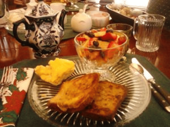 breakfast at a beautiful table showing a plate with french toast, scrambled eggs, and a dish with fruit