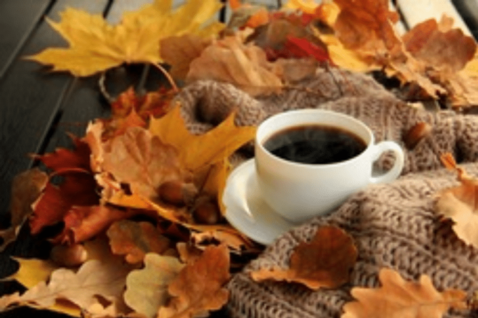 full cup of coffee sitting among fall leaves