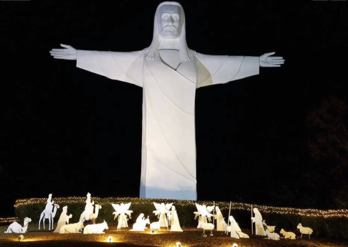 Statue of Christ with arms spread out and manger lighted up below