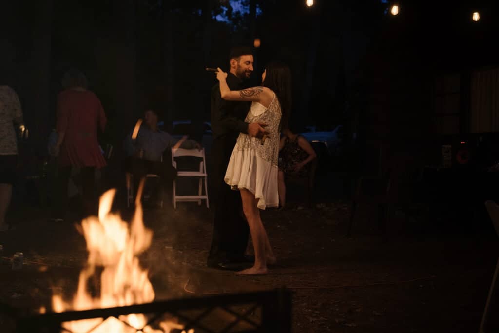 bride and groom dancing barefoot in front of a camp fire