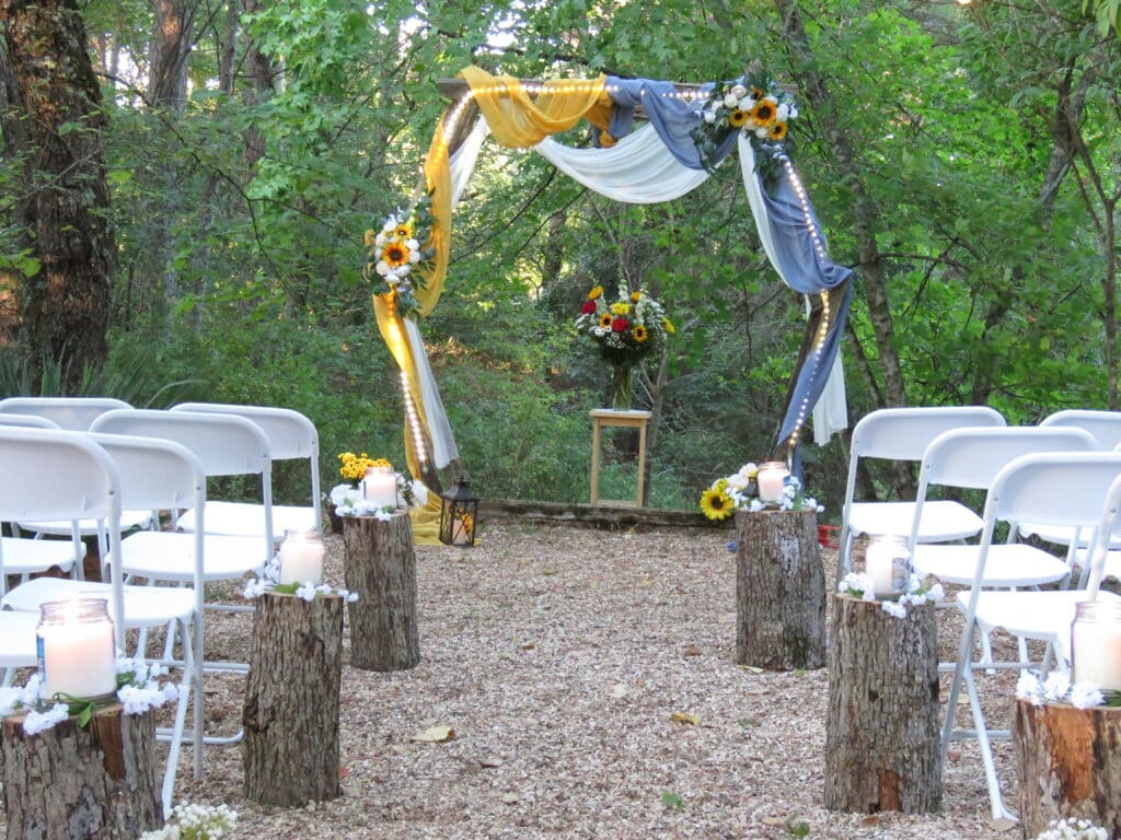 rustic wedding arch, decorated in colored drapes and white chairs sitting around it
