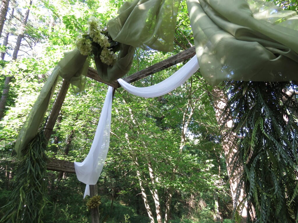 view of rustic wedding arch decorated in forest green drapes and flowers