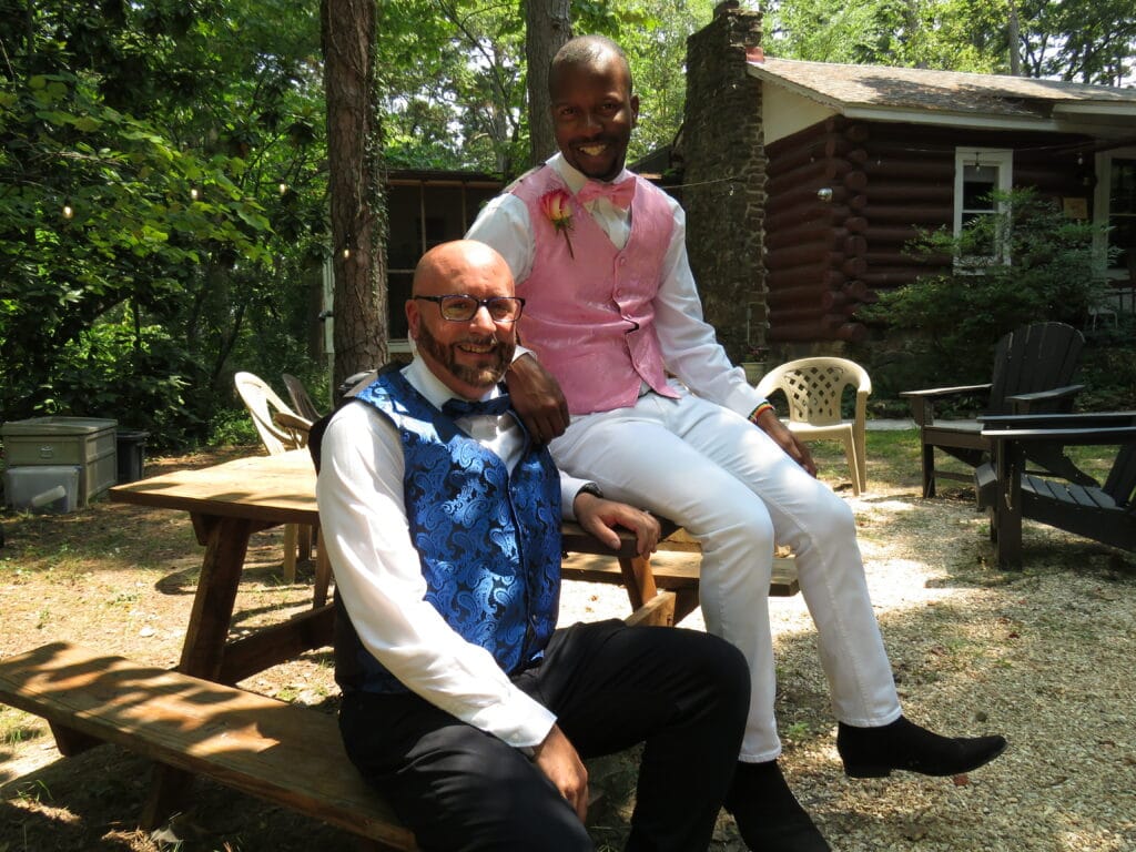 groom and groom posing on a rustic picnic table in front of a cabin