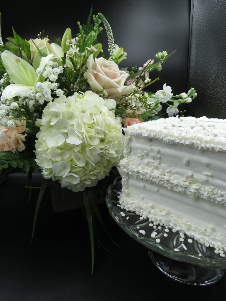 small white square wedding cake sitting next to a bridal bouquet of muted green and blush color