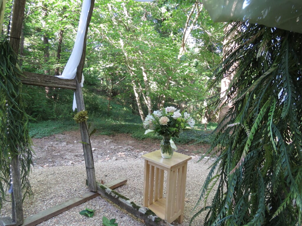 view of rustic wedding arch decorated in forest green drapes and flowers
