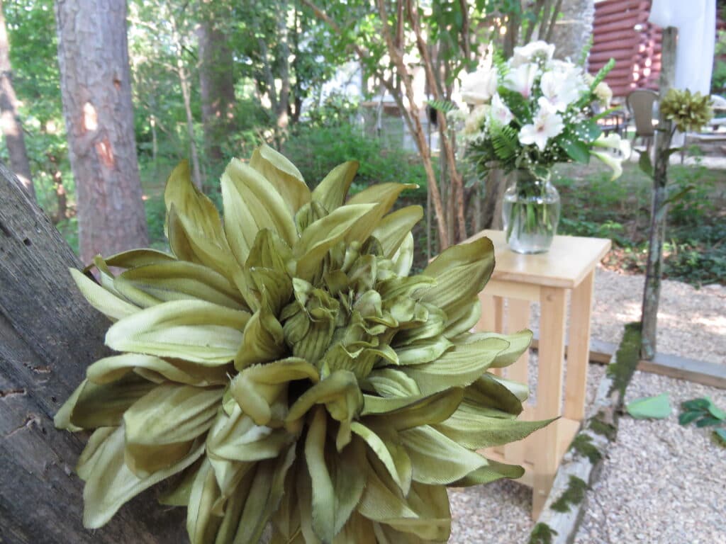 rustic wedding arch with green flower and wedding bouquet seen in background in muted green colors