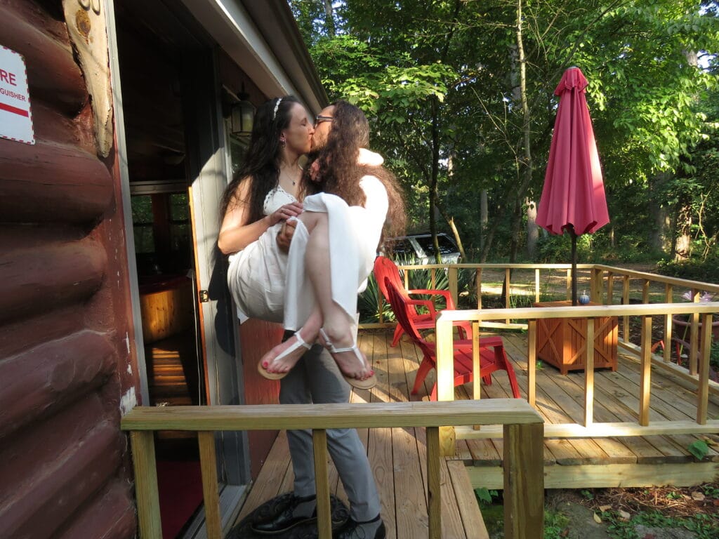 groom carrying bride over the threshold of a cabin while kissing