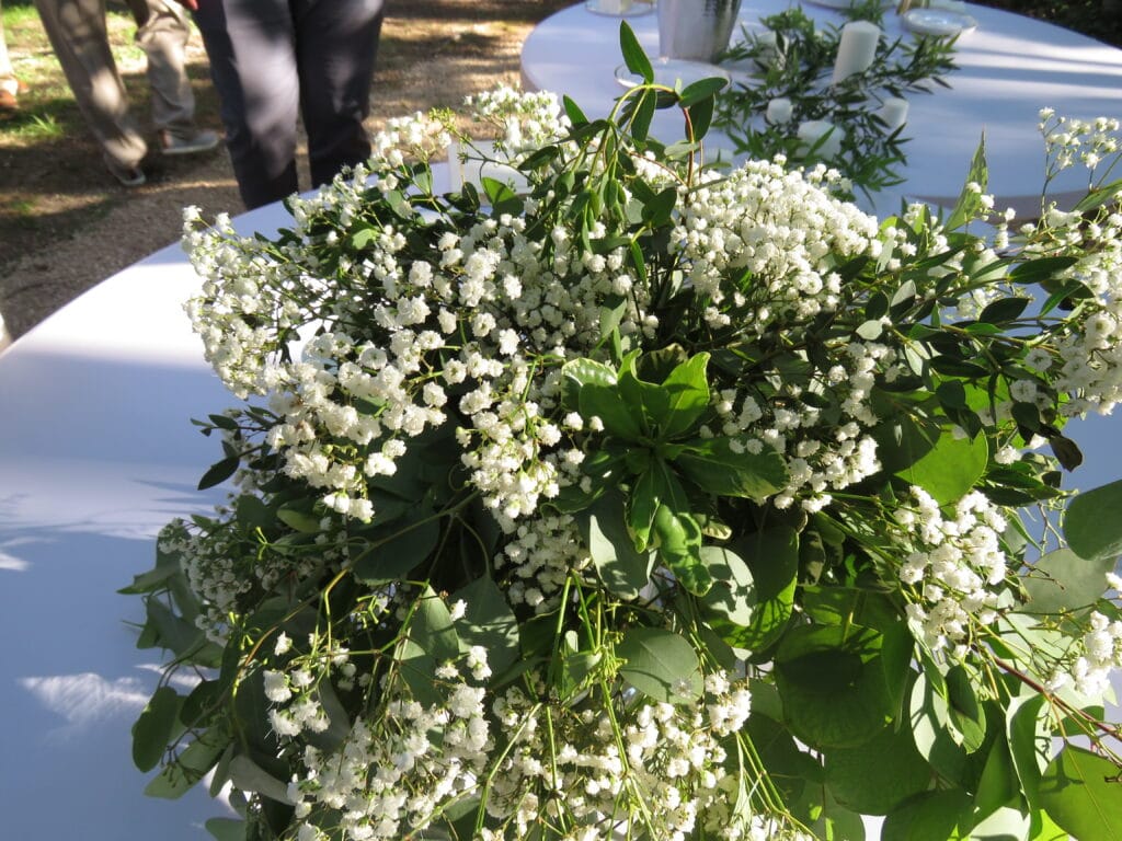 bridal bouquet with white round decorated tables shown in the background, tables are decorated in matching green foliage and white candles
