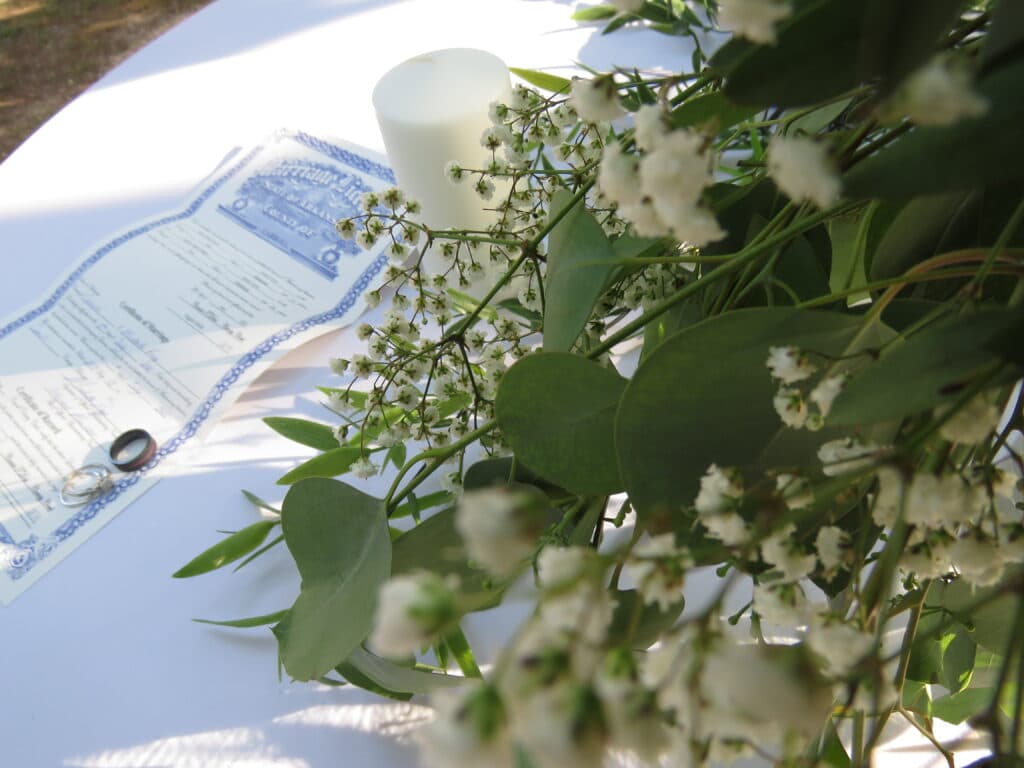 bridal bouquet in mixed green foliage with marriage license in background with wedding rings laying on it