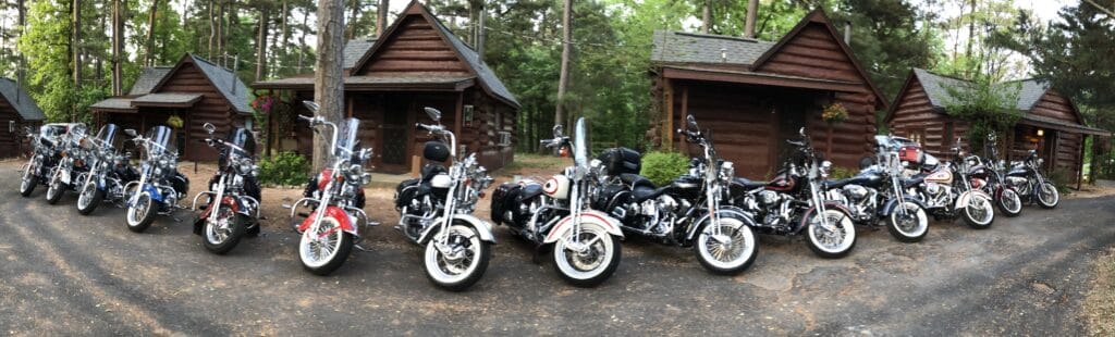 twenty motorcycles lined up in a row in front of old historic cabins