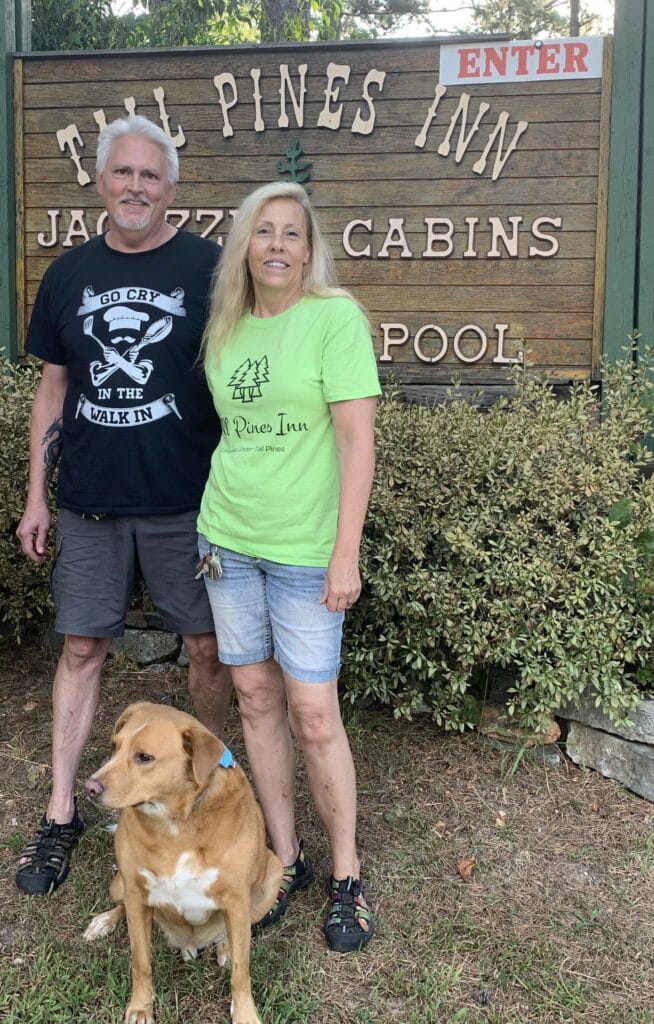 man woman and dog in front of an entrance sign