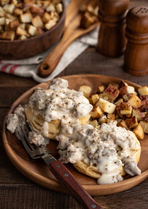 wooden dish with biscuits and sausage gravy with diced potatoes beside it