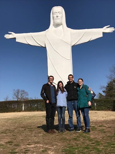 Large statue of christ of the ozark with four adults standing in front for a photo op
