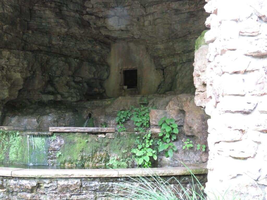 looking up into a cave in the side of a hill with concrete steps leading into it and surrounded by green vegetation